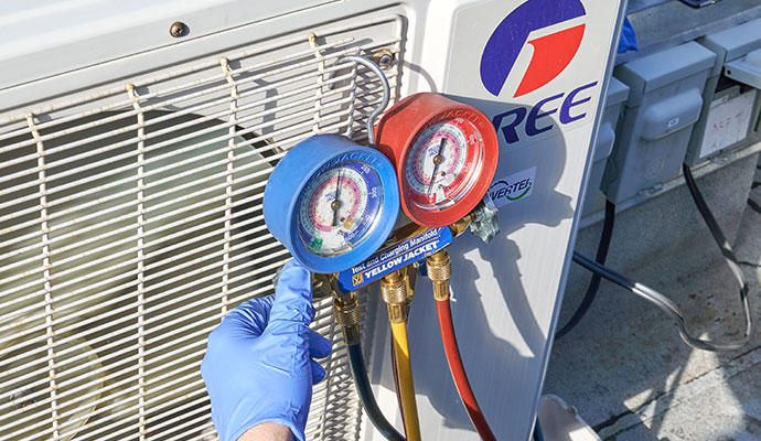 A technician using manifold gauges to check the pressure of an outdoor air conditioning condenser