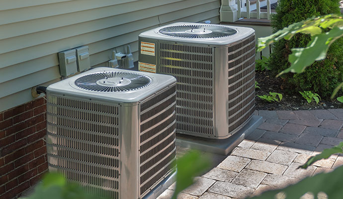 A pair of outdoor HVAC condenser units positioned on a clean backyard patio